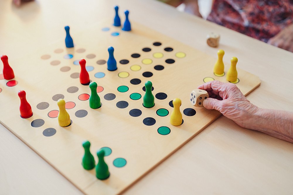 Ältere Hand setzt eine Spielfigur auf ein Brettspiel mit bunten Kegeln