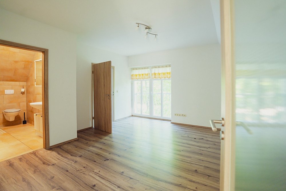 Frisch renovierte, leere Wohnung mit Laminatboden, bodentiefem Fenster und Blick ins geflieste Bad