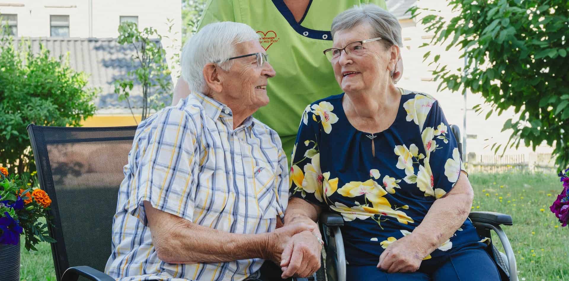 Ehepaar im Garten, begleitet von einer Pflegekraft
